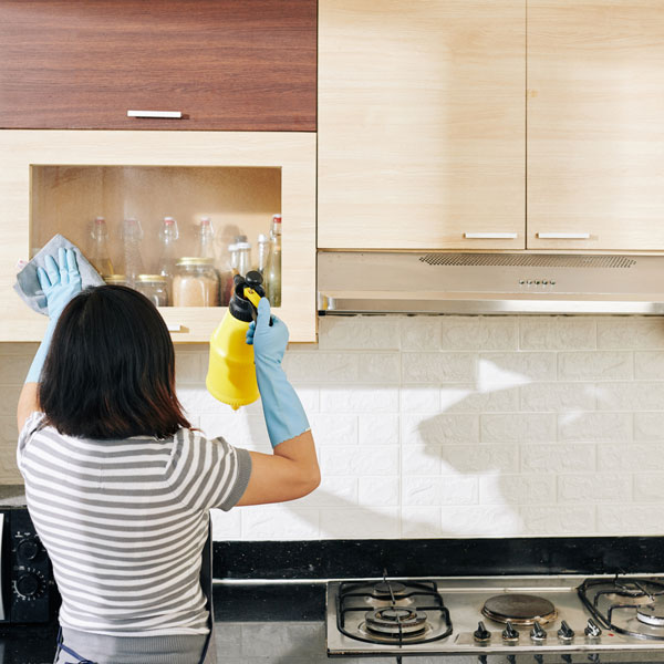 A woman cleaning the front of a glass panel cabinet in the kitchen