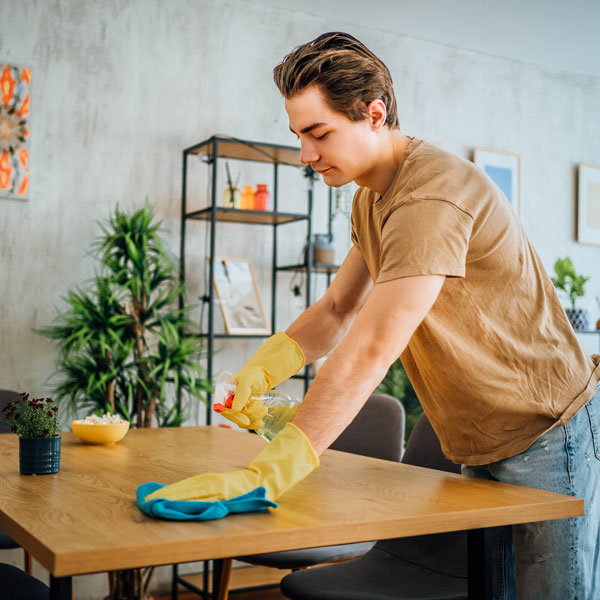 A man spraying cleaner on a wood table