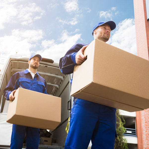 Two moving specialists carrying boxes from a loaded van into a home